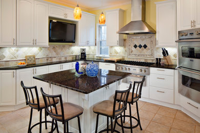 Large elegant u-shaped travertine floor eat-in kitchen photo in Omaha with raised-panel cabinets, white cabinets, beige backsplash, stainless steel appliances, granite countertops, stone tile backsplash and an island