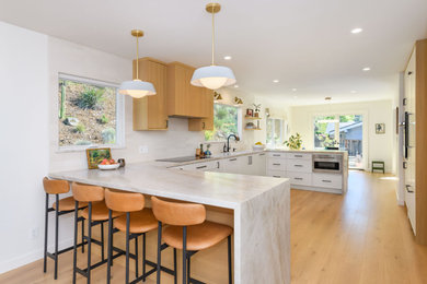 Example of a transitional u-shaped medium tone wood floor and brown floor kitchen design in San Francisco with an undermount sink, shaker cabinets, white cabinets, beige backsplash, stainless steel appliances, a peninsula and beige countertops