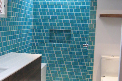 Inspiration for a mid-sized eclectic 3/4 blue tile and ceramic tile medium tone wood floor doorless shower remodel in Los Angeles with flat-panel cabinets, dark wood cabinets, a two-piece toilet, blue walls, an undermount sink and solid surface countertops