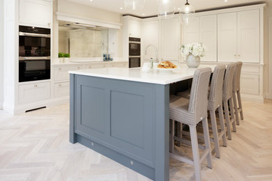 Inspiration for a traditional l-shaped kitchen/diner in Berkshire with a belfast sink, shaker cabinets, grey cabinets, engineered stone countertops, metallic splashback, mirror splashback, light hardwood flooring, an island, beige floors and white worktops.