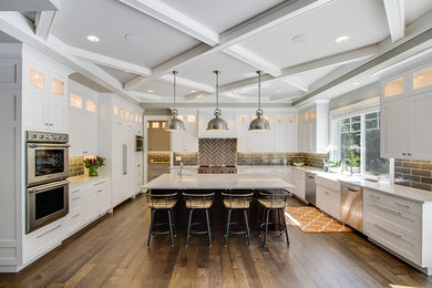 Photo of a large arts and crafts u-shaped eat-in kitchen in Seattle with a farmhouse sink, shaker cabinets, white cabinets, marble benchtops, grey splashback, ceramic splashback, stainless steel appliances, dark hardwood floors, with island and brown floor.