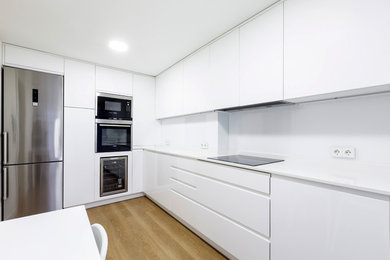 Inspiration for a mid-sized transitional l-shaped separate kitchen in Madrid with an undermount sink, flat-panel cabinets, white cabinets, quartz benchtops, white splashback, glass sheet splashback, stainless steel appliances, laminate floors, no island and brown floor.