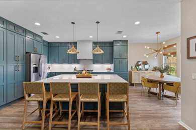 Inspiration for a mid-sized transitional l-shaped dark wood floor and brown floor eat-in kitchen remodel in Austin with an undermount sink, shaker cabinets, green cabinets, quartz countertops, white backsplash, ceramic backsplash, stainless steel appliances and white countertops
