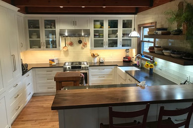 Eat-in kitchen - mid-sized transitional eat-in kitchen idea in Other with a farmhouse sink, white cabinets, quartz countertops, white backsplash, glass tile backsplash and stainless steel appliances