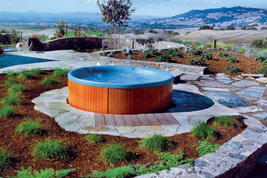 Tuscan backyard stone and round aboveground hot tub photo in Los Angeles