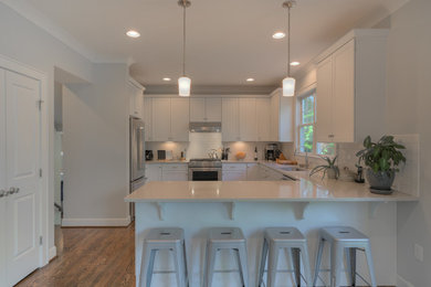 Enclosed kitchen - mid-sized craftsman l-shaped medium tone wood floor enclosed kitchen idea in DC Metro with an undermount sink, shaker cabinets, white cabinets, solid surface countertops, white backsplash, subway tile backsplash, stainless steel appliances and a peninsula