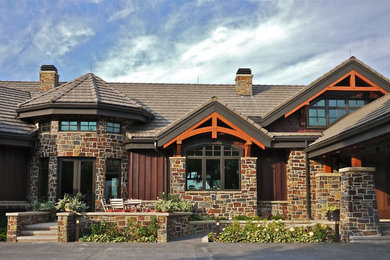 This is an example of a large arts and crafts two-storey brown exterior in Calgary with stone veneer and a gable roof.