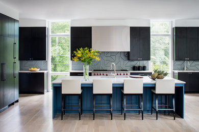 This is an example of a contemporary kitchen in DC Metro with an undermount sink, flat-panel cabinets, black cabinets, grey splashback, stainless steel appliances, light hardwood floors, with island, beige floor and white benchtop.