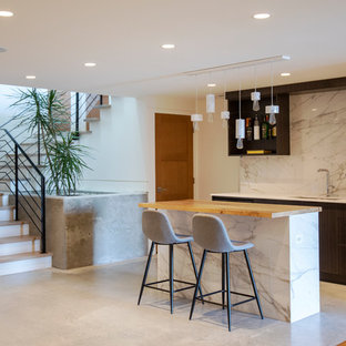 バンクーバーの中サイズのコンテンポラリースタイルのおしゃれな着席型バー (アンダーカウンターシンク、フラットパネル扉のキャビネット、黒いキャビネット、木材カウンター、白いキッチンパネル、大理石の床、コンクリートの床、グレーの床) の写真