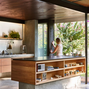 Idée de décoration pour une petite arrière-cuisine parallèle minimaliste avec un évier encastré, un placard à porte plane, des portes de placard en bois clair, un plan de travail en granite, une crédence blanche, un électroménager noir, béton au sol, un îlot central et un sol gris.