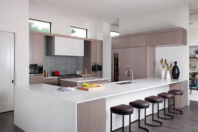 Photo of a contemporary l-shaped open plan kitchen in Orange County with a single-bowl sink, flat-panel cabinets, light wood cabinets, marble benchtops, grey splashback, mosaic tile splashback, stainless steel appliances, dark hardwood floors and multiple islands.