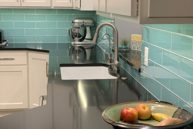Large trendy u-shaped light wood floor and brown floor kitchen photo in Other with an undermount sink, flat-panel cabinets, white cabinets, quartzite countertops, green backsplash, glass tile backsplash, stainless steel appliances, an island and black countertops