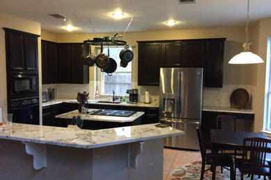 Mid-sized transitional l-shaped porcelain tile and beige floor eat-in kitchen photo in Austin with an undermount sink, recessed-panel cabinets, black cabinets, marble countertops, white backsplash, marble backsplash, stainless steel appliances, an island and white countertops