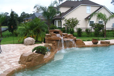 This is an example of a mid-sized transitional backyard custom-shaped lap pool in Jacksonville with a water feature and brick pavers.