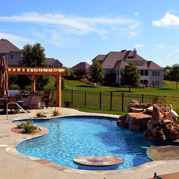Free form pool with stone table, sun shelf, water feature, and outdoor kitchen,