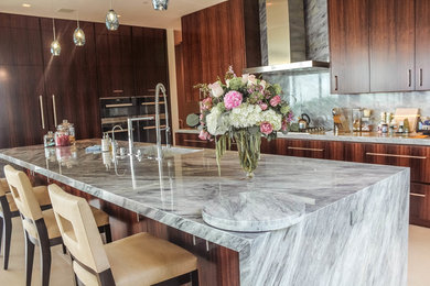 Eat-in kitchen - large modern l-shaped beige floor and travertine floor eat-in kitchen idea in Los Angeles with an integrated sink, flat-panel cabinets, dark wood cabinets, granite countertops, gray backsplash, stone slab backsplash, stainless steel appliances, an island and gray countertops