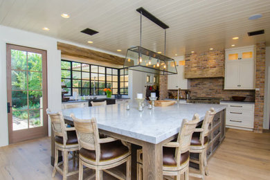 Example of a mid-sized classic l-shaped light wood floor eat-in kitchen design in Phoenix with a farmhouse sink, raised-panel cabinets, white cabinets, red backsplash, stainless steel appliances, an island and marble countertops