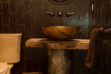 Powder room - rustic brown tile and glass tile powder room idea in New York with a vessel sink, wood countertops, a one-piece toilet, brown walls and brown countertops