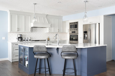 Example of a large transitional l-shaped medium tone wood floor and brown floor open concept kitchen design in Calgary with an undermount sink, recessed-panel cabinets, gray cabinets, quartzite countertops, white backsplash, ceramic backsplash, stainless steel appliances and an island