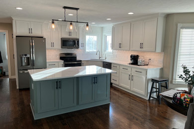 Kitchen - contemporary dark wood floor and brown floor kitchen idea in Omaha with an undermount sink, flat-panel cabinets, white cabinets, solid surface countertops, white backsplash, ceramic backsplash, stainless steel appliances, an island and white countertops