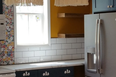 Inspiration for a mid-sized shabby-chic style l-shaped laminate floor and gray floor eat-in kitchen remodel in Other with a farmhouse sink, flat-panel cabinets, blue cabinets, laminate countertops, white backsplash, ceramic backsplash, white appliances, an island and white countertops