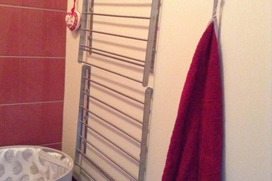 Imagen de armario lavadero lineal actual de tamaño medio con paredes rojas, suelo de baldosas de cerámica y lavadora y secadora juntas
