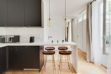 パリにある高級な中くらいなコンテンポラリースタイルのおしゃれなキッチン (アンダーカウンターシンク、インセット扉のキャビネット、黒いキャビネット、大理石カウンター、白いキッチンパネル、大理石のキッチンパネル、黒い調理設備、淡色無垢フローリング、ベージュの床、白いキッチンカウンター) の写真