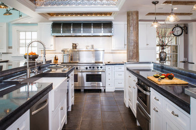 Inspiration for a timeless u-shaped kitchen remodel in New York with a farmhouse sink, shaker cabinets, white cabinets, white backsplash, subway tile backsplash, stainless steel appliances, two islands and black countertops