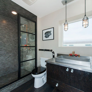 Idées déco pour une salle de bain industrielle avec un placard à porte plane, un WC séparé, carrelage en mosaïque, un mur beige, un sol en bois foncé, une vasque, un plan de toilette en acier inoxydable, des portes de placard noires, un carrelage gris et une cabine de douche à porte battante.