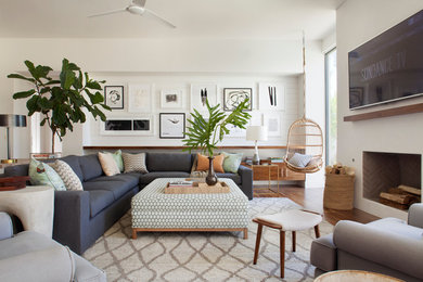Large beach style open concept medium tone wood floor family room photo in Los Angeles with white walls, a standard fireplace, a plaster fireplace and a wall-mounted tv
