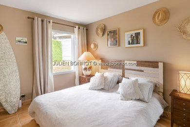 Aménagement d'une chambre d'amis beige et blanche exotique avec un mur beige, tomettes au sol et un sol orange.