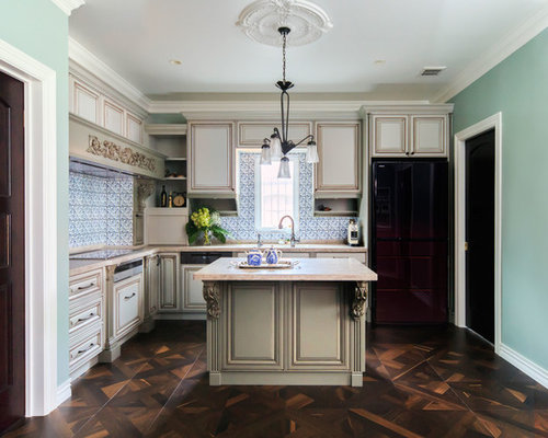 東京23区の広いL型ヴィクトリアンなダイニングキッチンの写真 (アンダーカウンターシンク、レイズドパネル扉のキャビネット、ベージュのキャビネット、オニキスカウンター、青いキッチンパネル、ガラスタイルのキッチンパネル、黒い調理設備、無垢フローリング、アイランド1つ)