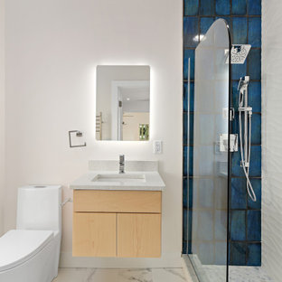 Foto di una piccola stanza da bagno con doccia minimalista con ante lisce, ante in legno chiaro, doccia alcova, WC monopezzo, piastrelle blu, piastrelle bianche, piastrelle in gres porcellanato, pareti bianche, pavimento con piastrelle di ciottoli, lavabo sottopiano, pavimento grigio, doccia aperta e top bianco