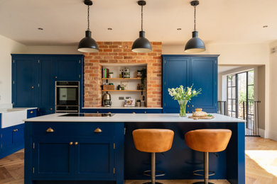 This is an example of a large contemporary open plan kitchen in Buckinghamshire with a belfast sink, shaker cabinets, blue cabinets, granite worktops, black appliances, vinyl flooring, an island and white worktops.