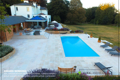 This is an example of an expansive contemporary back formal full sun garden in Hampshire with a retaining wall and concrete paving.
