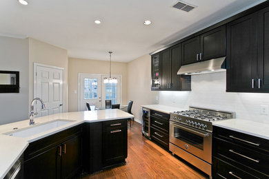 Example of a transitional l-shaped medium tone wood floor eat-in kitchen design in Dallas with an undermount sink, shaker cabinets, dark wood cabinets, solid surface countertops, subway tile backsplash, stainless steel appliances, no island and white backsplash