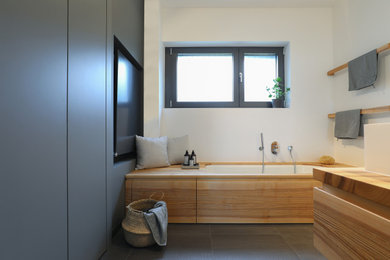 Photo of a mid-sized modern master bathroom in Frankfurt with flat-panel cabinets, light wood cabinets, an undermount tub, a curbless shower, a one-piece toilet, gray tile, white walls, a vessel sink, solid surface benchtops, grey floor, a shower curtain, a niche, a double vanity and a floating vanity.