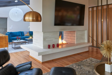 Example of a large 1960s open concept medium tone wood floor, brown floor and vaulted ceiling family room design in Seattle with white walls, a two-sided fireplace, a stacked stone fireplace and a wall-mounted tv