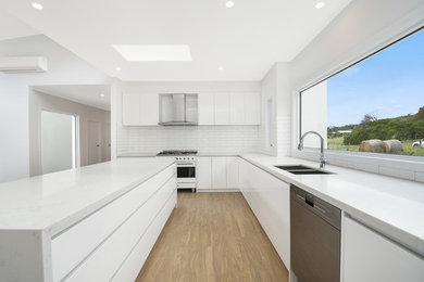 Photo of a mid-sized modern eat-in kitchen in Melbourne with white cabinets, quartz benchtops, white splashback, subway tile splashback, stainless steel appliances, vinyl floors, with island, white benchtop and an undermount sink.