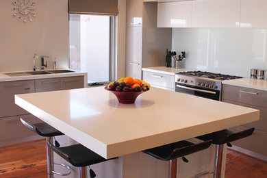 This is an example of a mid-sized modern u-shaped eat-in kitchen in Perth with a double-bowl sink, flat-panel cabinets, white cabinets, concrete benchtops, white splashback, glass sheet splashback, stainless steel appliances, dark hardwood floors and with island.