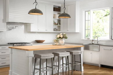 Inspiration for a large transitional l-shaped open plan kitchen in Austin with a farmhouse sink, shaker cabinets, white cabinets, quartzite benchtops, white splashback, ceramic splashback, stainless steel appliances, light hardwood floors, with island and grey floor.