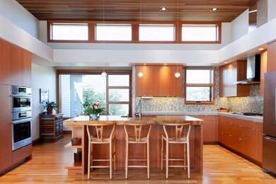 Inspiration for a mid-sized contemporary l-shaped medium tone wood floor kitchen remodel in Other with flat-panel cabinets, medium tone wood cabinets, concrete countertops, multicolored backsplash, glass tile backsplash, stainless steel appliances, an island and gray countertops