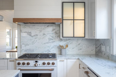 Mid-sized eclectic kitchen in Raleigh with a farmhouse sink, shaker cabinets, white cabinets, quartzite benchtops, white splashback, engineered quartz splashback, white appliances, medium hardwood floors, with island, brown floor, white benchtop and exposed beam.