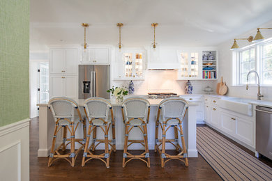 Example of a classic l-shaped dark wood floor and brown floor kitchen design in Baltimore with a farmhouse sink, recessed-panel cabinets, white cabinets, white backsplash, subway tile backsplash, stainless steel appliances, an island and white countertops