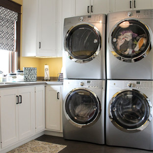 Inspiration for a large traditional u-shaped separated utility room with a single-bowl sink, recessed-panel cabinets, white cabinets, composite countertops, yellow walls, porcelain flooring and a stacked washer and dryer.