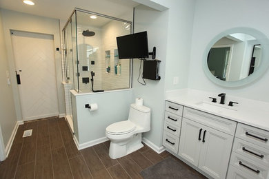 Photo of a master bathroom in Indianapolis with recessed-panel cabinets, white cabinets, a corner shower, white tile, cement tile, white walls, a drop-in sink, engineered quartz benchtops, brown floor, a hinged shower door and white benchtops.