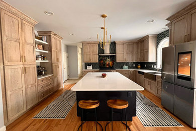 Mid-sized transitional l-shaped medium tone wood floor and brown floor enclosed kitchen photo in Other with a farmhouse sink, recessed-panel cabinets, light wood cabinets, quartz countertops, black backsplash, mosaic tile backsplash, stainless steel appliances, an island and white countertops