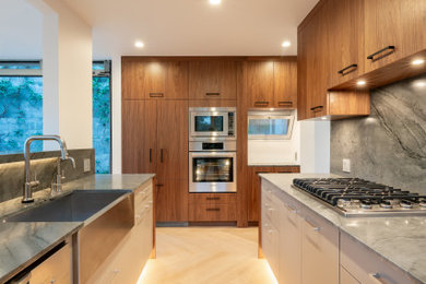 Minimalist light wood floor kitchen photo in Los Angeles with a farmhouse sink, flat-panel cabinets, dark wood cabinets and gray backsplash