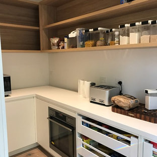 Cette image montre une arrière-cuisine parallèle minimaliste de taille moyenne avec un évier encastré, des portes de placard blanches, un plan de travail en quartz modifié, une crédence en dalle de pierre, un électroménager en acier inoxydable, un sol en bois clair et un îlot central.