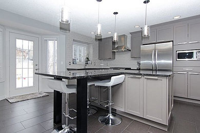 Example of a mid-sized trendy l-shaped porcelain tile kitchen design in Calgary with an undermount sink, shaker cabinets, gray cabinets, granite countertops, gray backsplash, ceramic backsplash, stainless steel appliances and an island